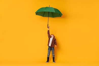 Little boy with green umbrella on orange background