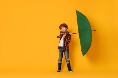 Little boy with green umbrella on orange background, space for text