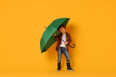 Photo of Little boy with green umbrella on orange background