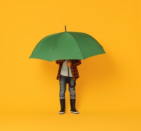 Little boy with green umbrella on orange background