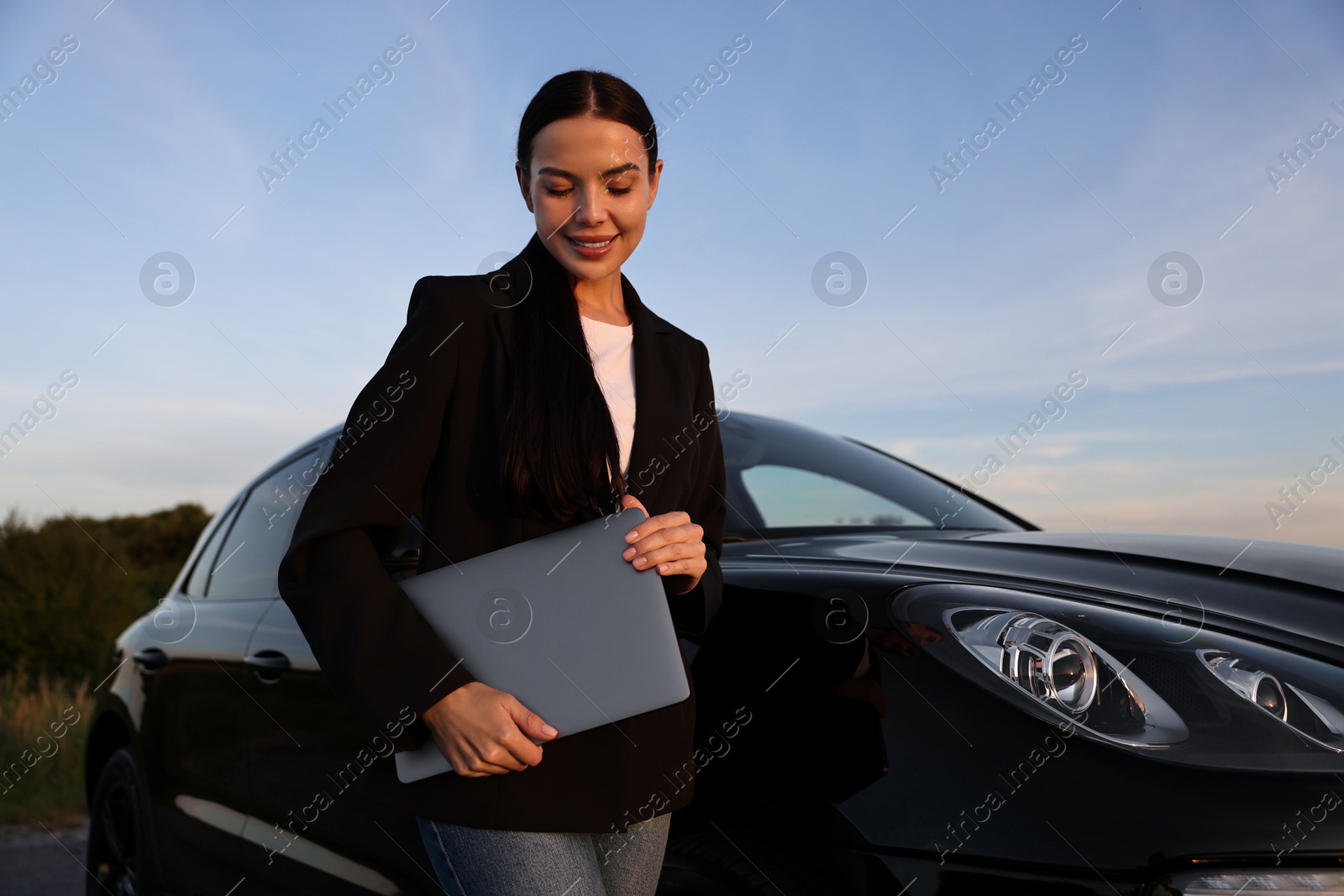 Photo of Happy young woman with laptop near car outdoors