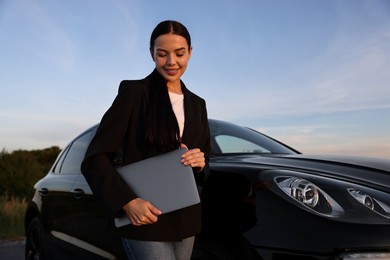 Happy young woman with laptop near car outdoors