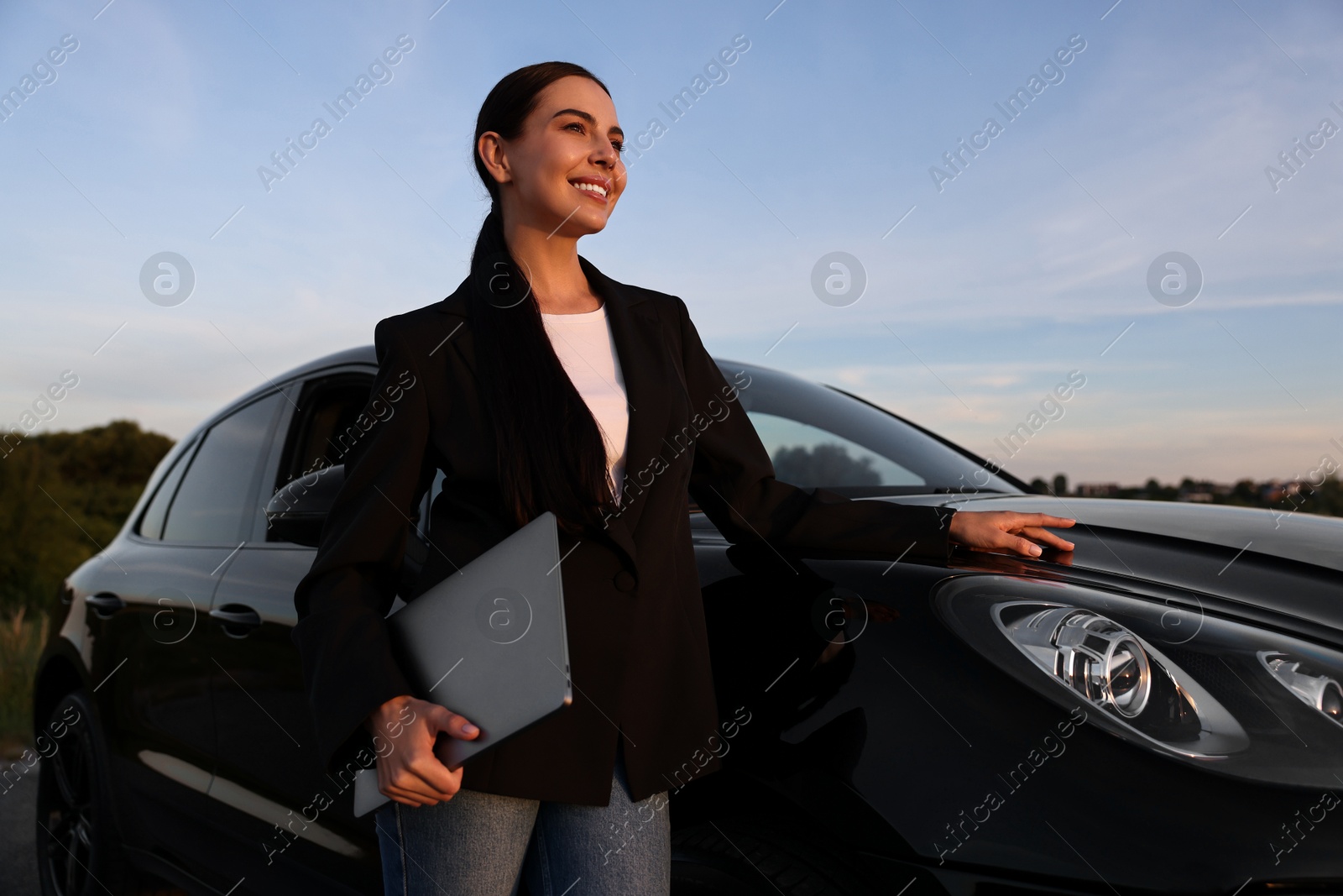 Photo of Happy young woman with laptop near car outdoors