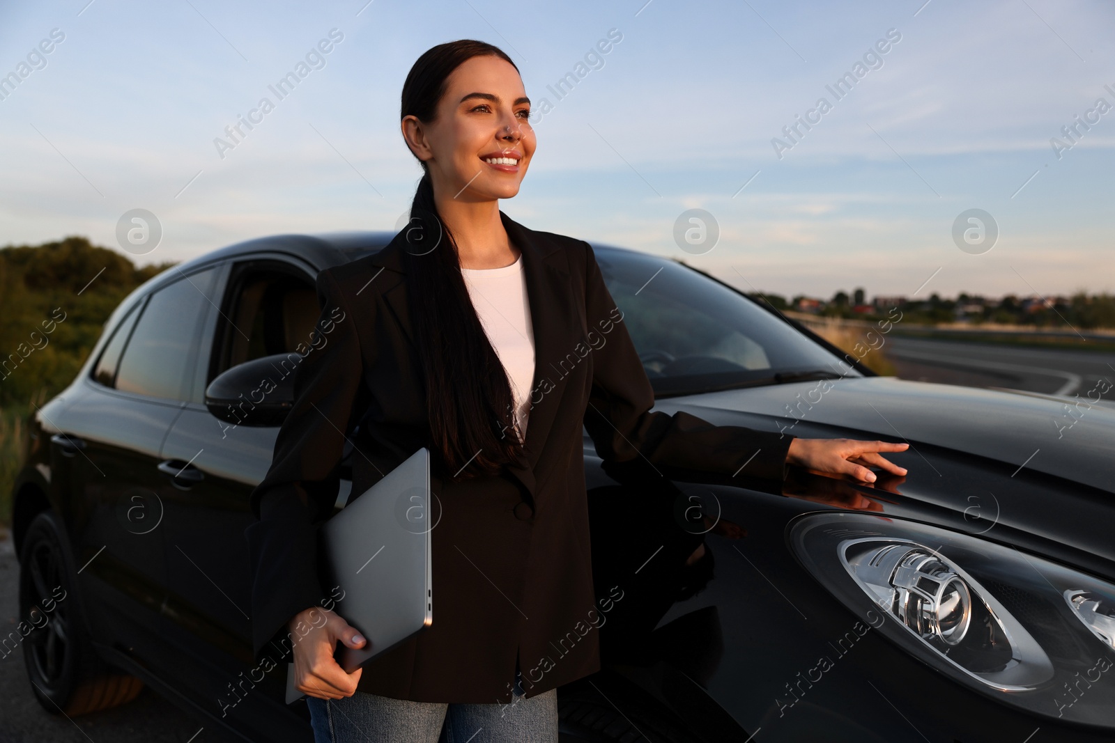 Photo of Happy young woman with laptop near car outdoors