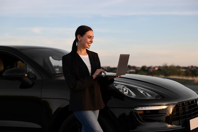 Happy young woman using laptop near car outdoors