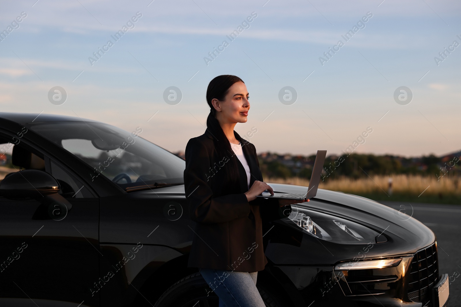 Photo of Beautiful young woman using laptop near car outdoors