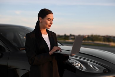 Photo of Beautiful young woman using laptop near car outdoors