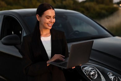 Happy young woman using laptop near car outdoors