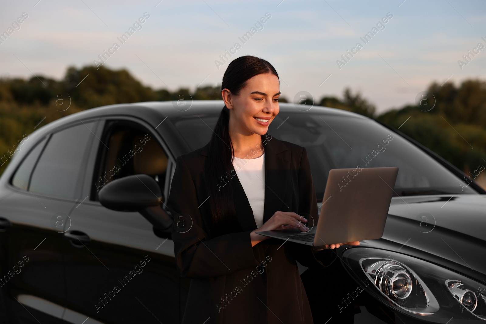 Photo of Happy young woman using laptop near car outdoors