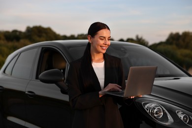 Happy young woman using laptop near car outdoors