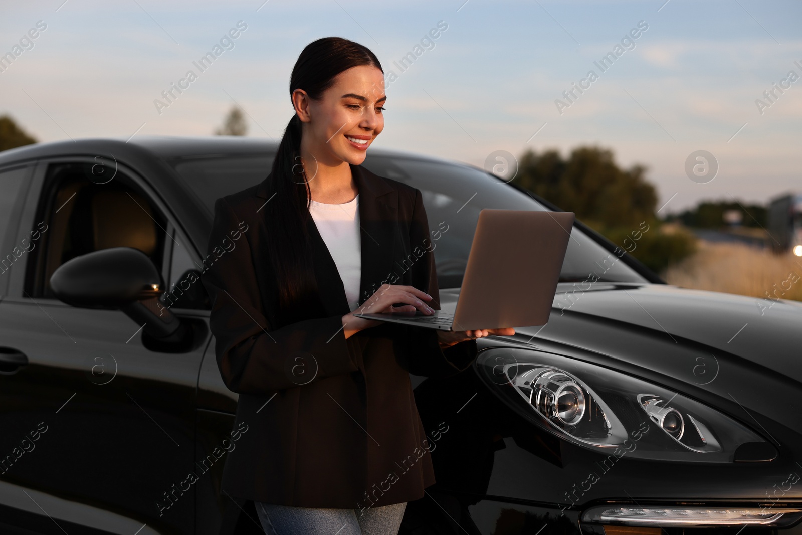 Photo of Happy young woman using laptop near car outdoors