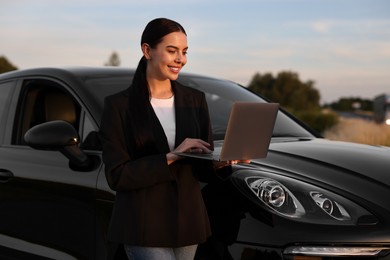 Happy young woman using laptop near car outdoors