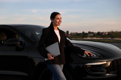 Happy young woman with laptop near car outdoors