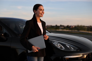 Happy young woman with laptop near car outdoors