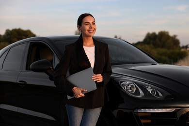 Happy young woman with laptop near car outdoors