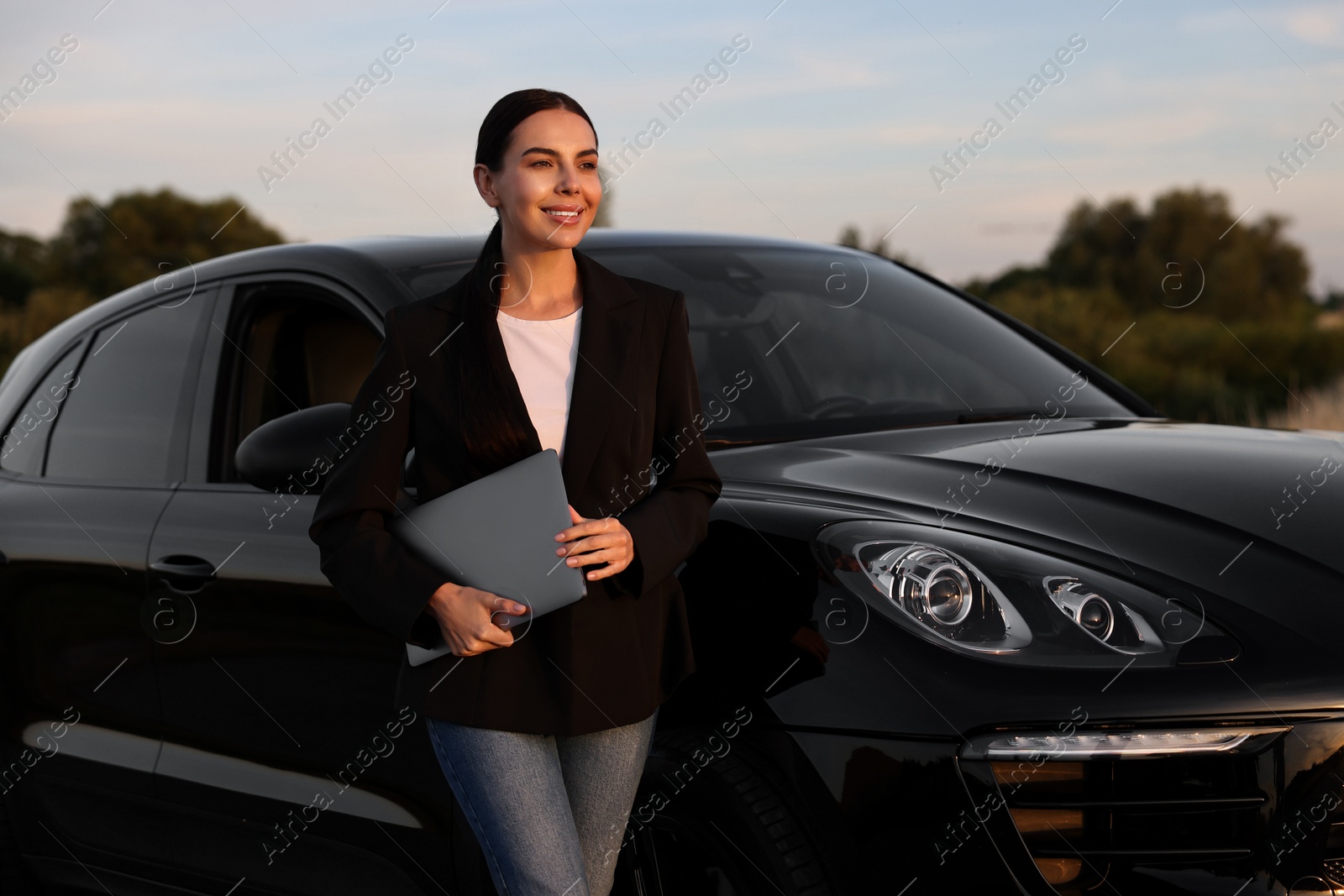 Photo of Happy young woman with laptop near car outdoors