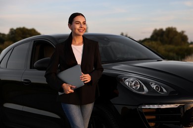 Happy young woman with laptop near car outdoors