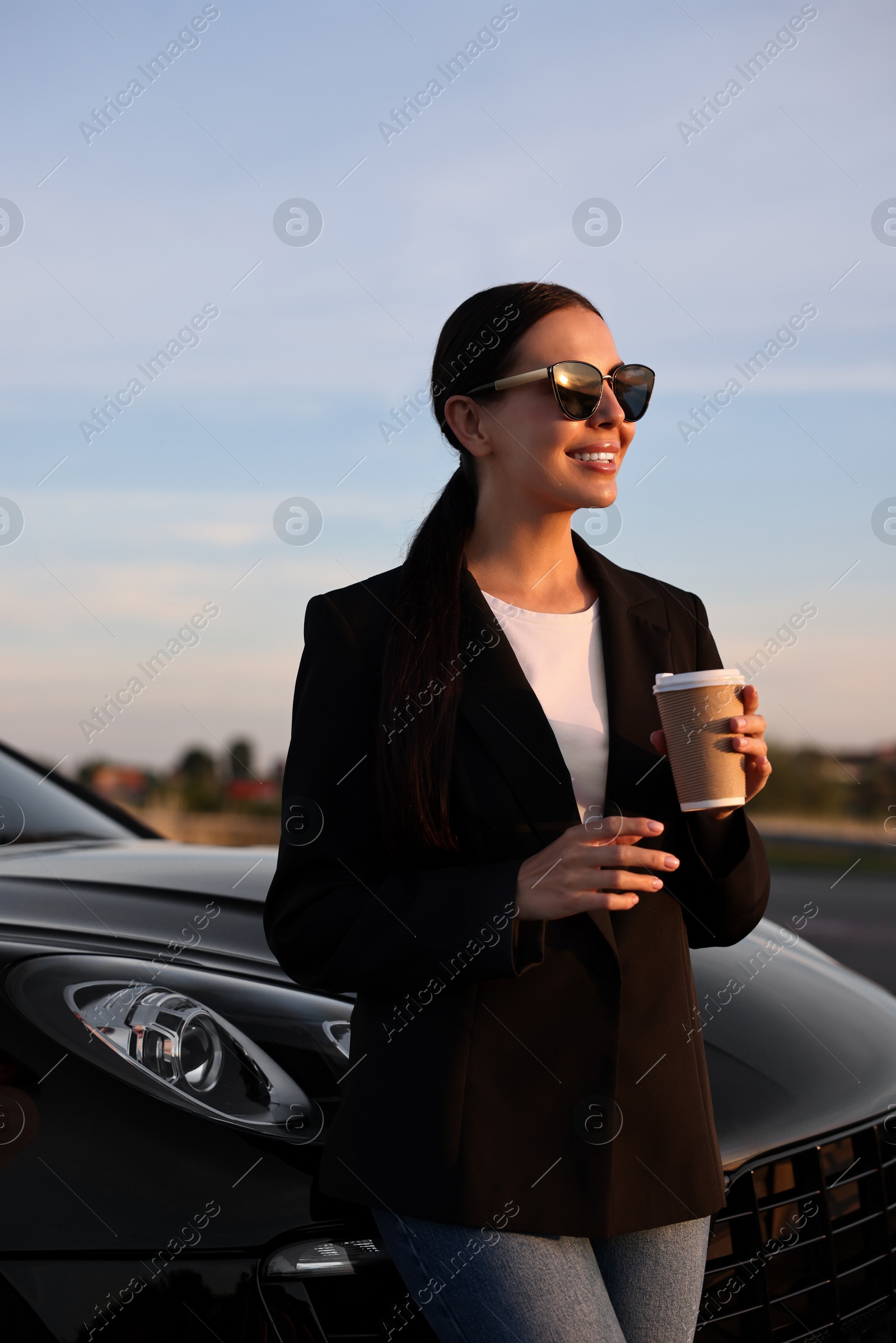 Photo of Smiling woman in sunglasses with paper cup of drink near car outdoors