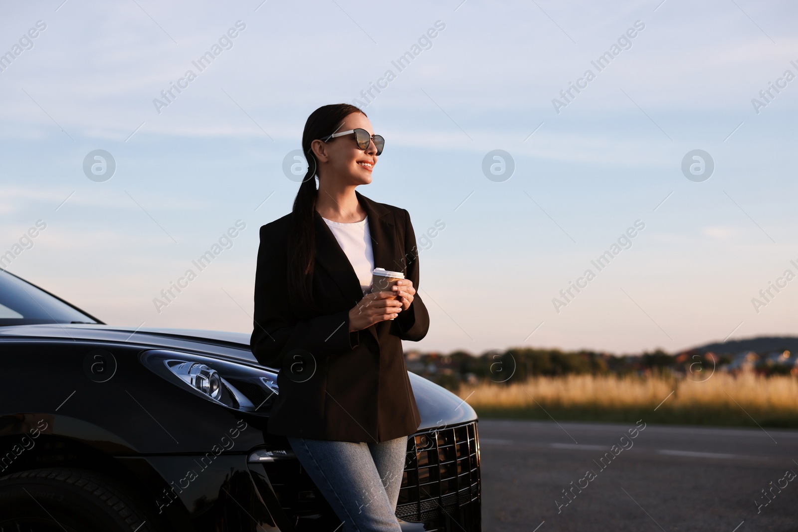 Photo of Smiling woman in sunglasses with paper cup of drink near car outdoors