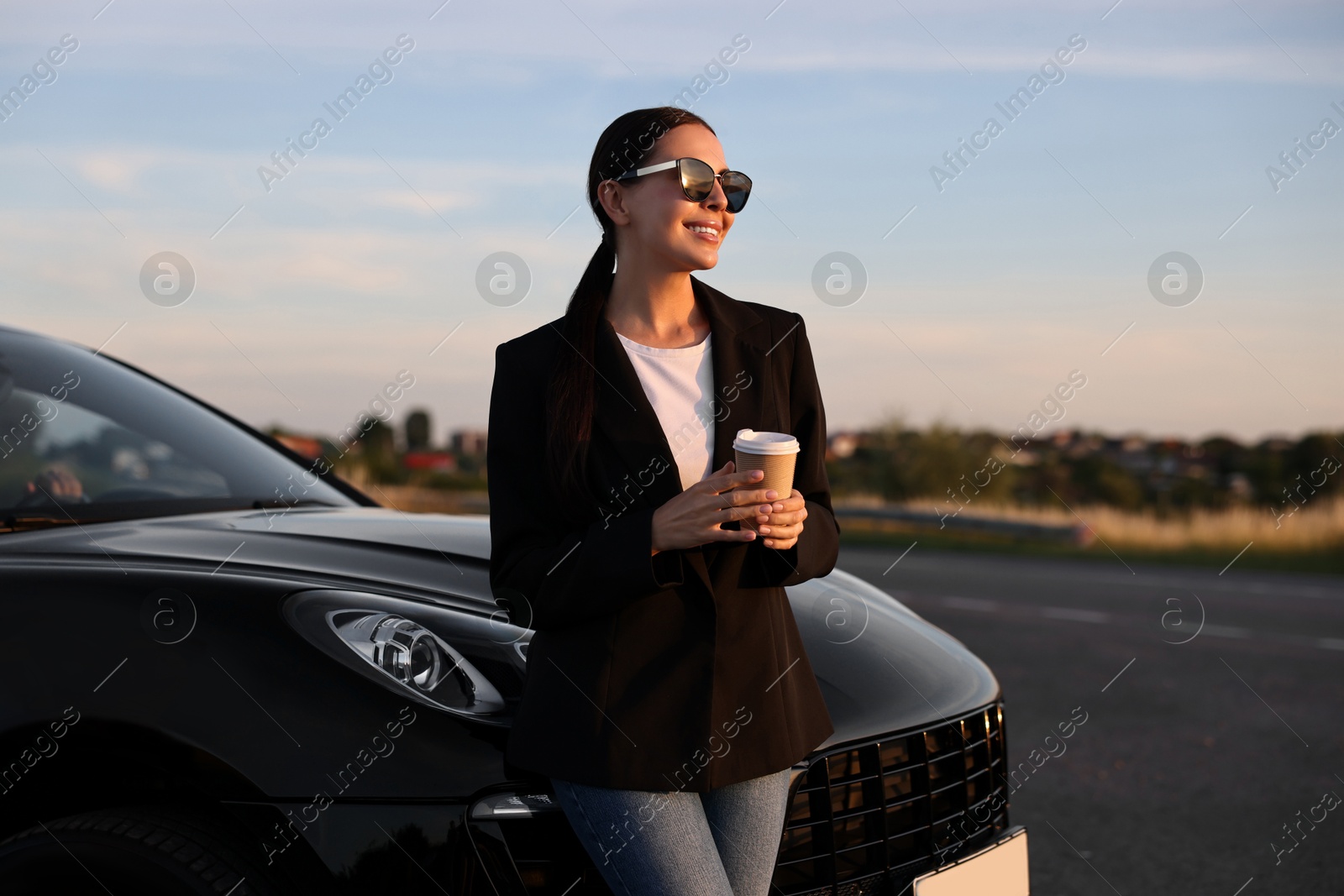 Photo of Smiling woman in sunglasses with paper cup of drink near car outdoors