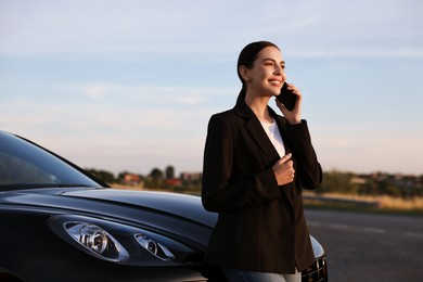 Photo of Smiling young woman talking on smartphone near car outdoors