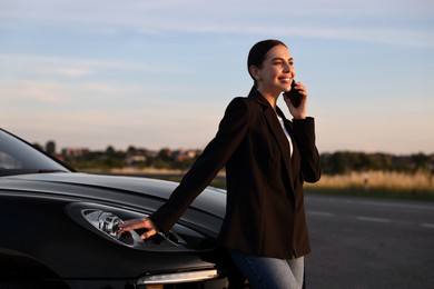 Smiling young woman talking on smartphone near car outdoors