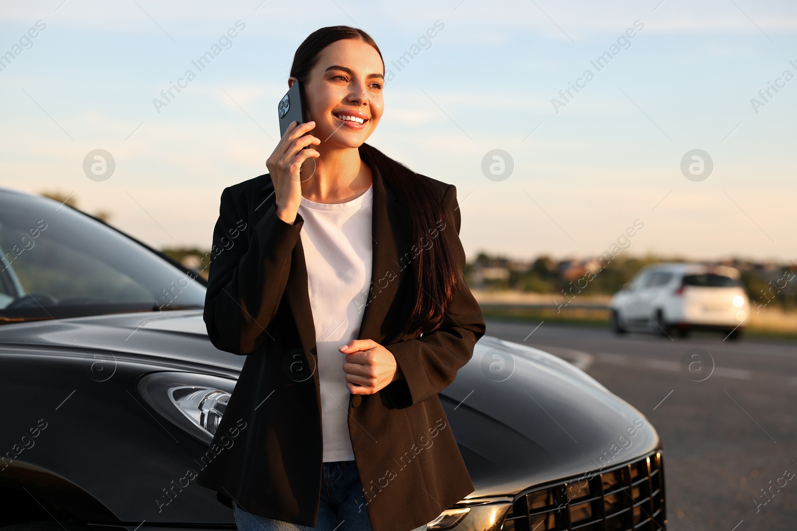 Photo of Smiling young woman talking on smartphone near car outdoors