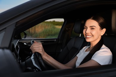 Smiling young woman holding steering wheel while driving car, view from outside