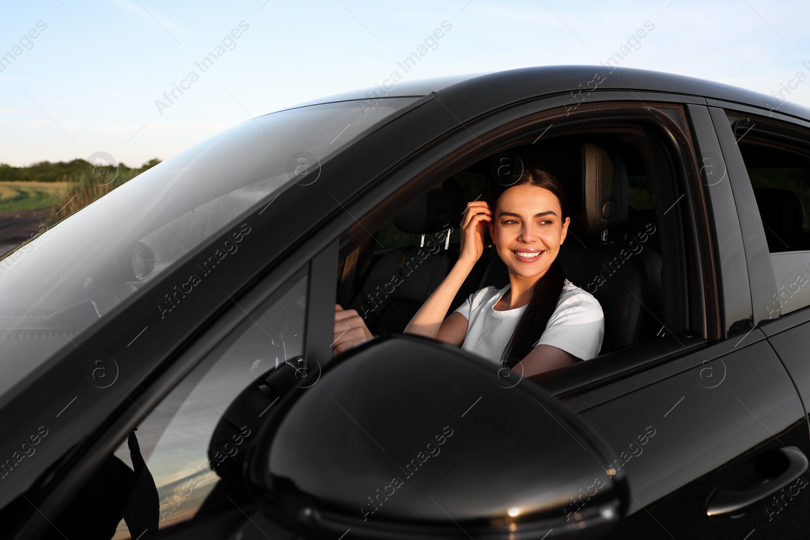 Photo of Smiling young woman holding steering wheel while driving car, view from outside