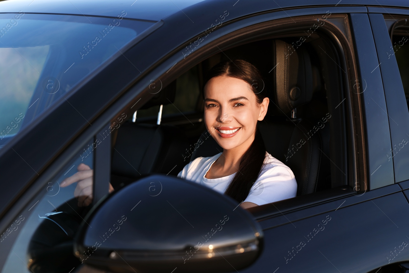 Photo of Smiling young woman holding steering wheel while driving car, view from outside