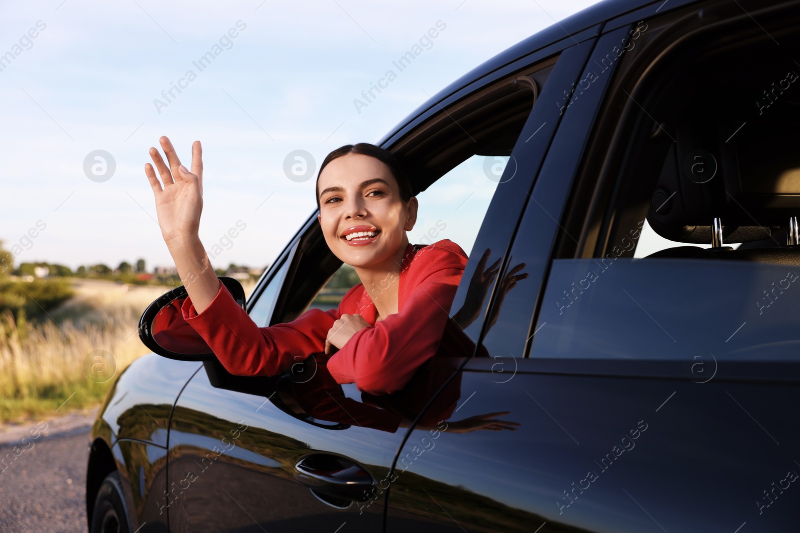 Photo of Smiling young woman leaning out of car window, view from outside. Enjoying trip