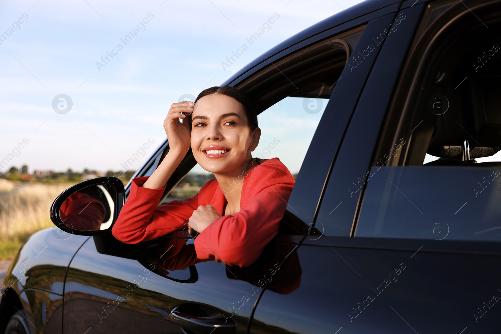 Photo of Smiling young woman leaning out of car window, view from outside. Enjoying trip