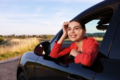 Photo of Smiling young woman leaning out of car window, view from outside. Enjoying trip