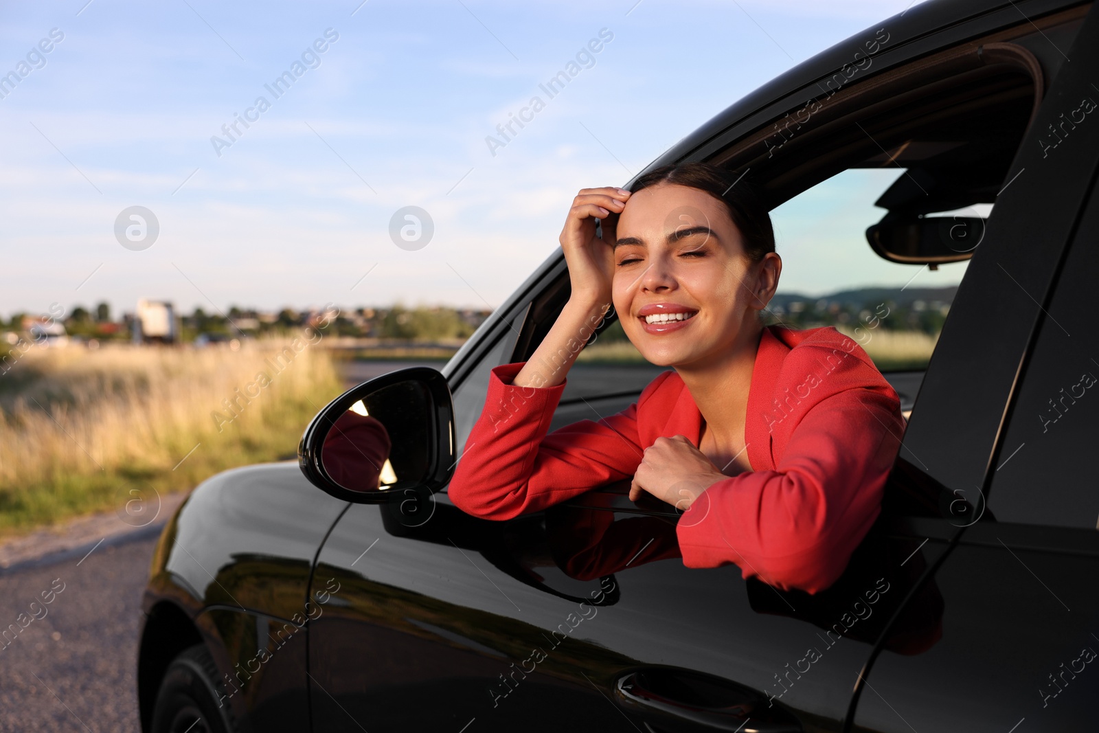 Photo of Smiling young woman leaning out of car window, view from outside. Enjoying trip