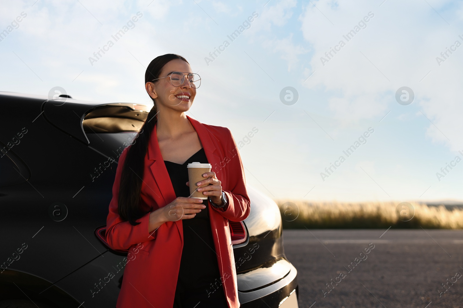 Photo of Smiling young woman with paper cup of drink near car outdoors, space for text