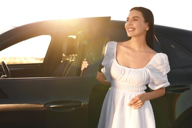 Smiling young woman near car at sunset