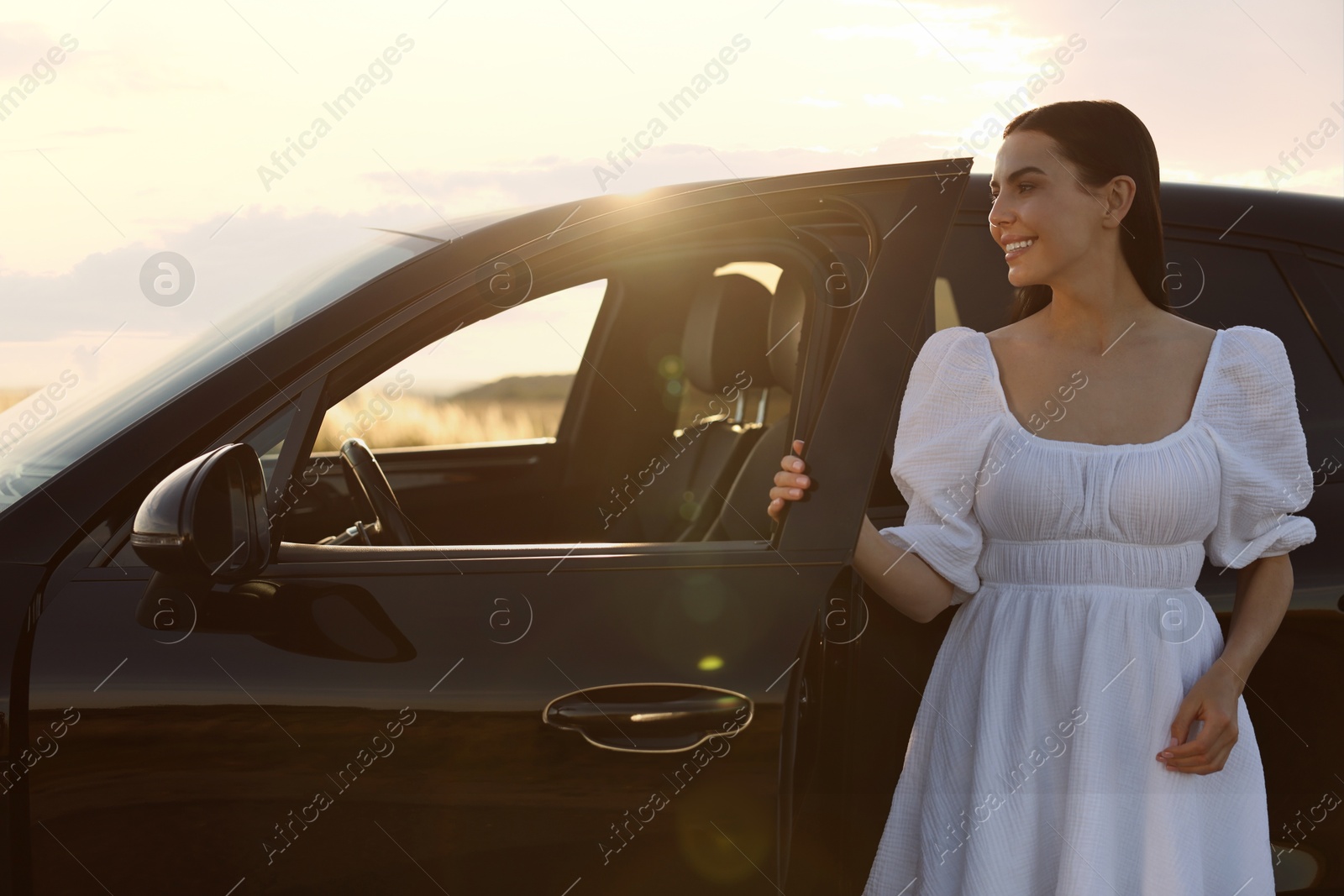 Photo of Smiling young woman near car at sunset