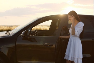 Smiling young woman near car at sunset