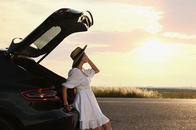 Photo of Woman in hat near trunk of car at sunset, space for text