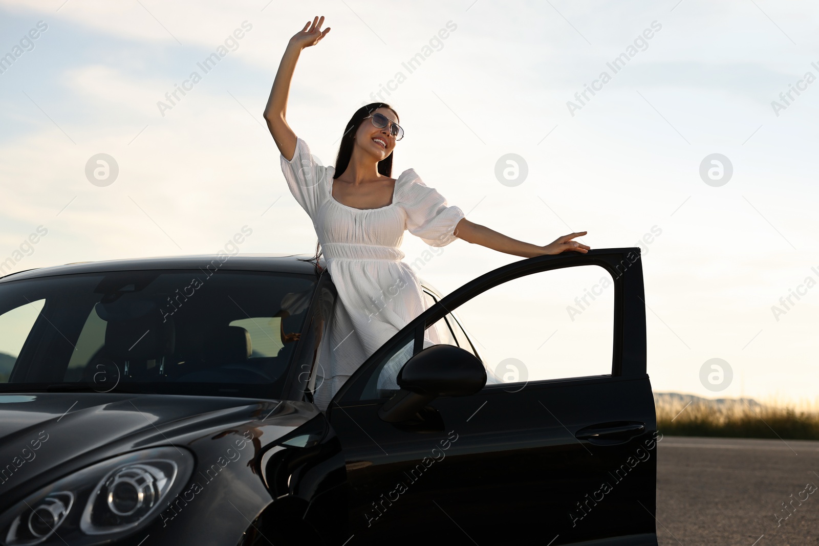 Photo of Smiling young woman in sunglasses leaning out of car outdoors. Enjoying trip