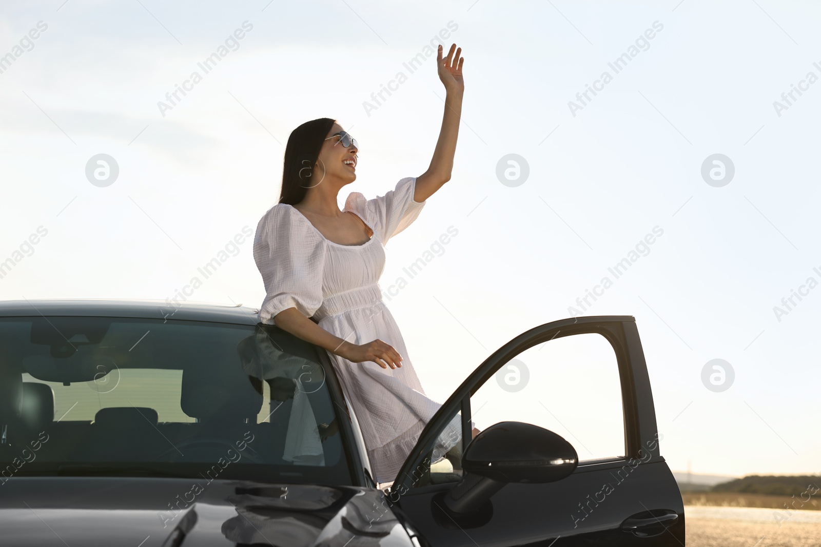 Photo of Smiling young woman in sunglasses leaning out of car outdoors. Enjoying trip