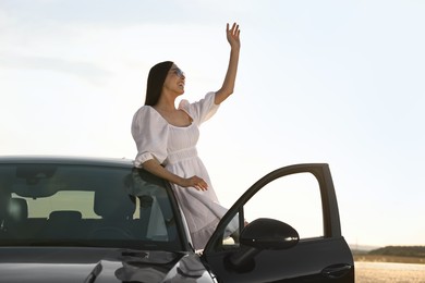 Smiling young woman in sunglasses leaning out of car outdoors. Enjoying trip