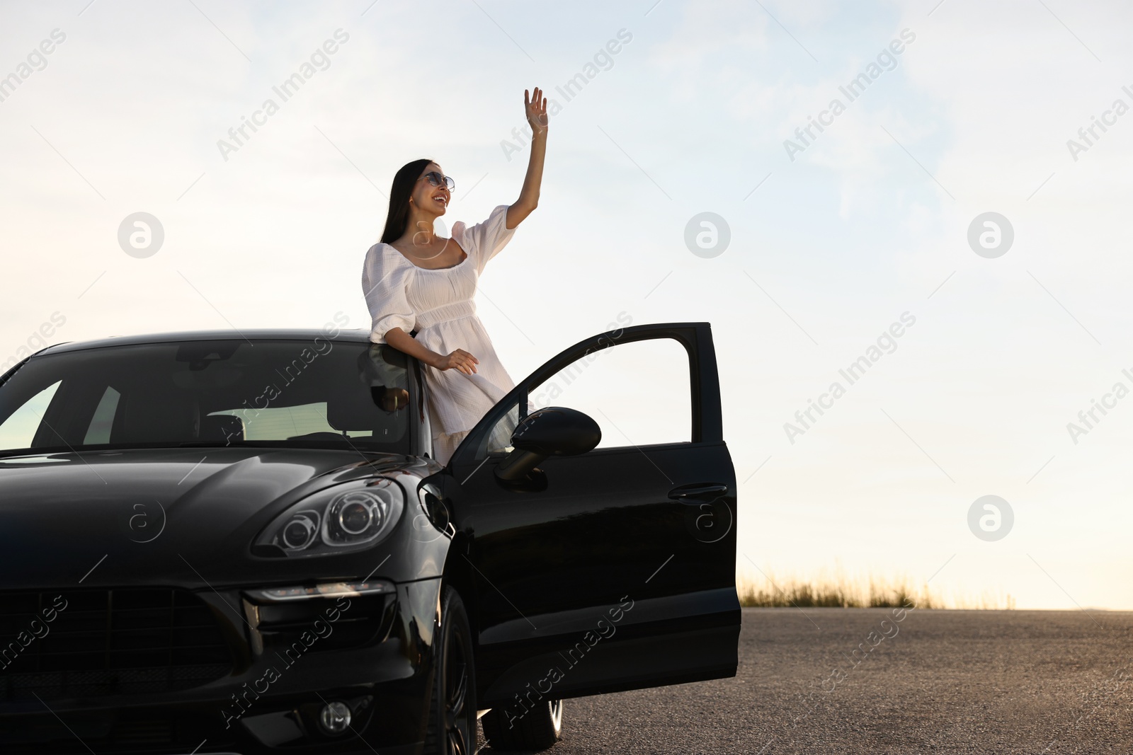 Photo of Smiling young woman in sunglasses leaning out of car outdoors. Enjoying trip