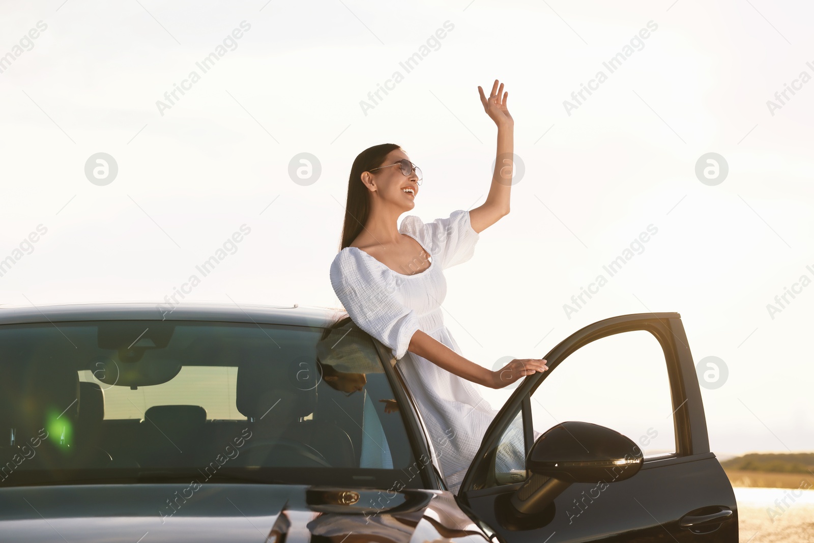 Photo of Smiling young woman in sunglasses leaning out of car outdoors. Enjoying trip