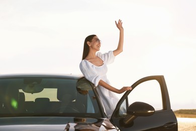 Photo of Smiling young woman in sunglasses leaning out of car outdoors. Enjoying trip