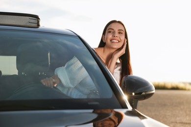 Smiling young woman leaning out of car window outdoors. Enjoying trip