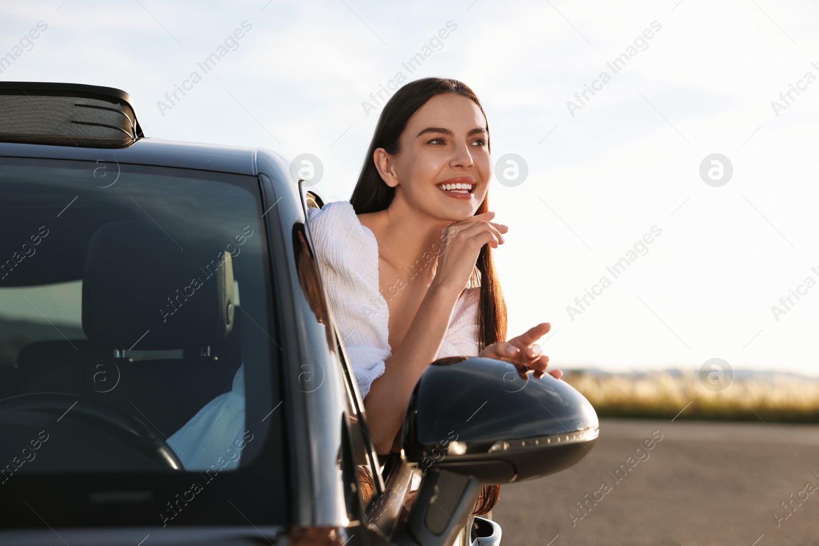 Photo of Smiling young woman leaning out of car window outdoors. Enjoying trip