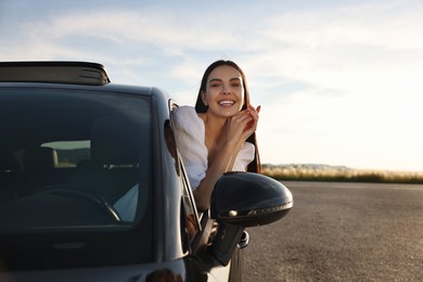 Photo of Smiling young woman leaning out of car window outdoors. Enjoying trip