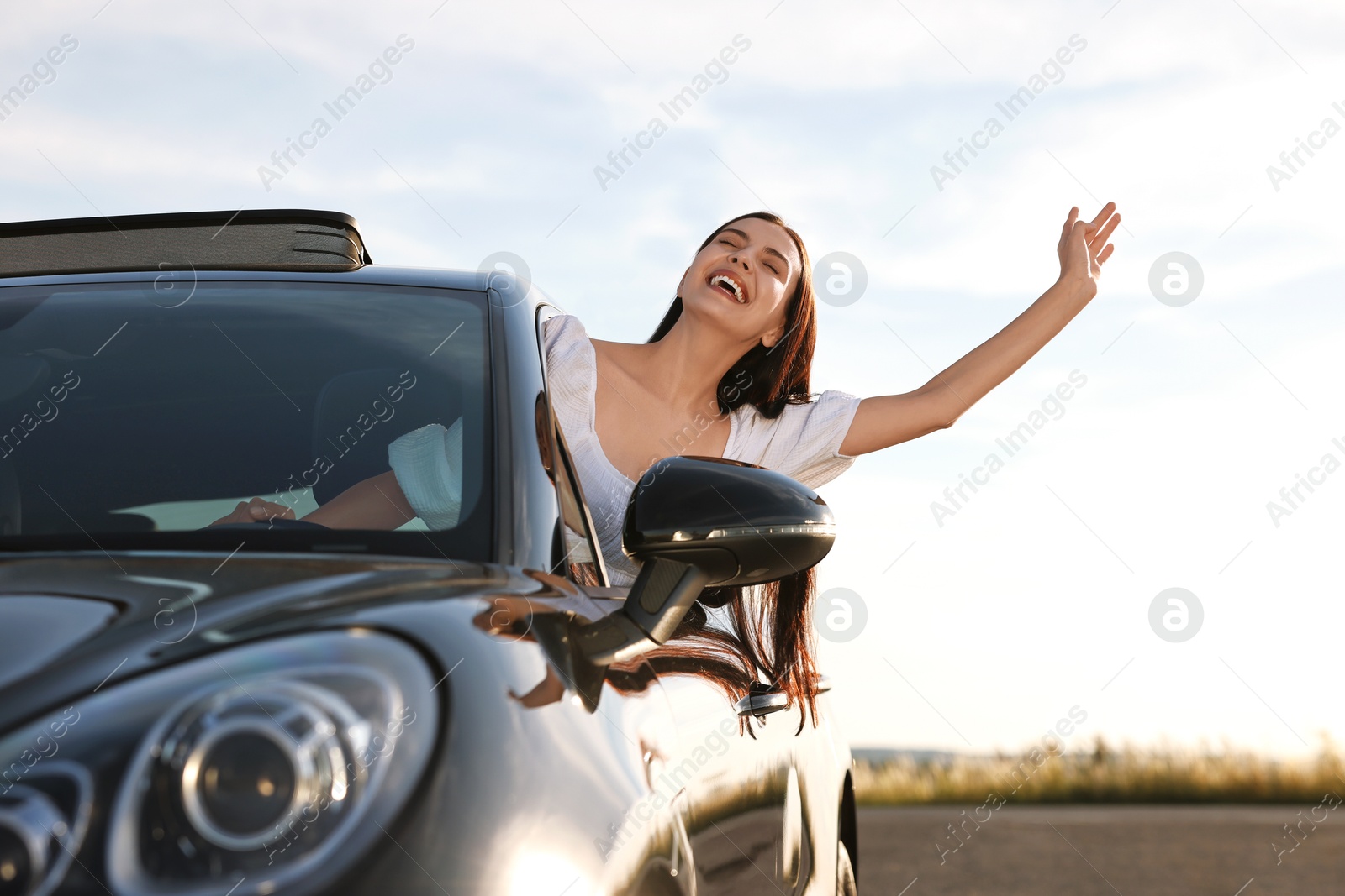 Photo of Smiling young woman leaning out of car window outdoors, low angle view. Enjoying trip