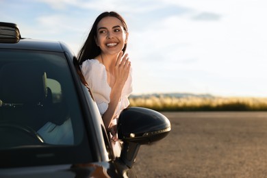 Smiling young woman leaning out of car window outdoors. Enjoying trip